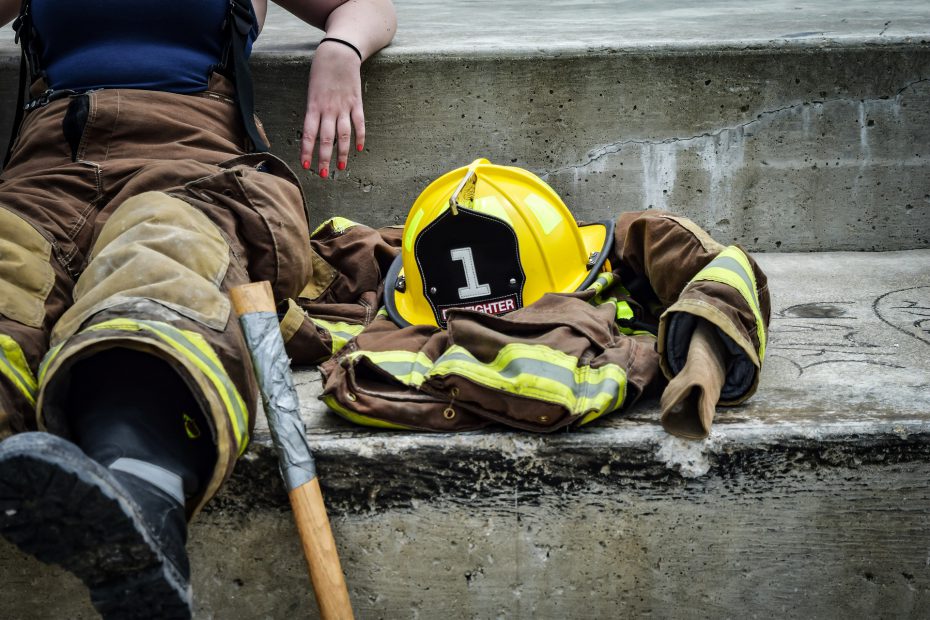 A firefighter sits on the ground next to their equipment.